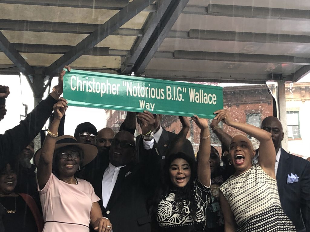 group of people hold the christopher wallace way street sign